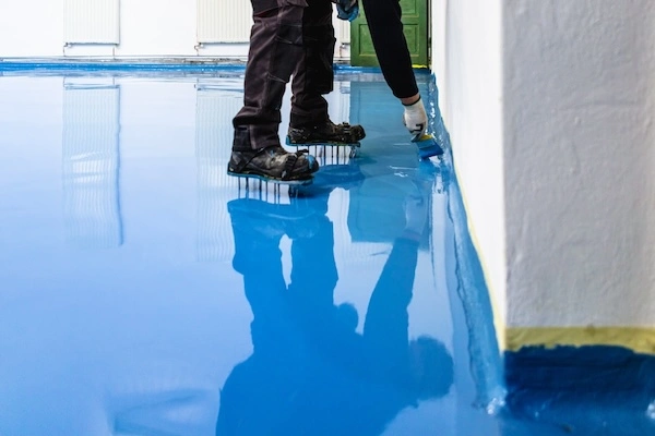 Worker Applying Blue Epoxy Coaoting to Concreet Floor.